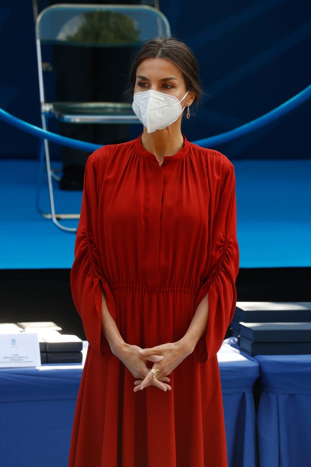 la reina, con un vestido rojo plisado y de manga larga, con moño y salones en color nude