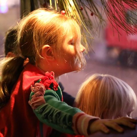 little blonde girl in christmas pjs looking out the train window, with her brother beside her, there is christmas greenery decorating the area above them