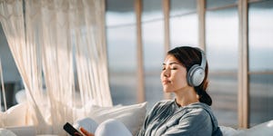 relaxed young asian woman with eyes closed sitting on her bed enjoying music over headphones from smartphone at home