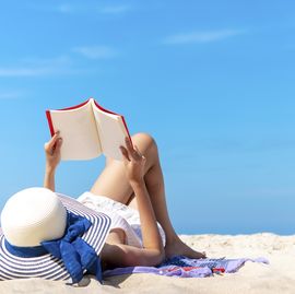 relaxing woman laying to read a book on the beach with blue sky in sunny day summer. happy travel and vacation times.