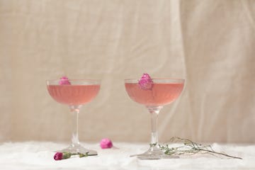 sparkling pink celebration drinks are shown in two vintage style champagne glasses and decorated with pink blossoms party bubbly or cocktails for friends or a romantic date, shot from the side to see the beautiful shape of the glass goblets