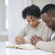 anniversary bible verses  man and woman with hands clasped praying together over bible