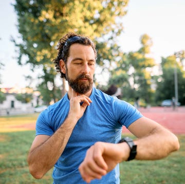 reloj deportivo inteligente hombre un hombre consulta su reloj deportivo inteligente mientras mide sus pulsaciones en el cuello con la mano