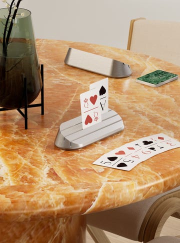 playing cards in a cast aluminum holder, on a marbled yellow table and next to a vase