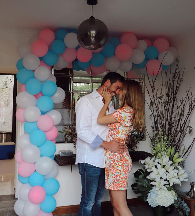 juan diego covarrubias y renata haro se sonríen bajo un arco de globos de colores blanco azul y rosa