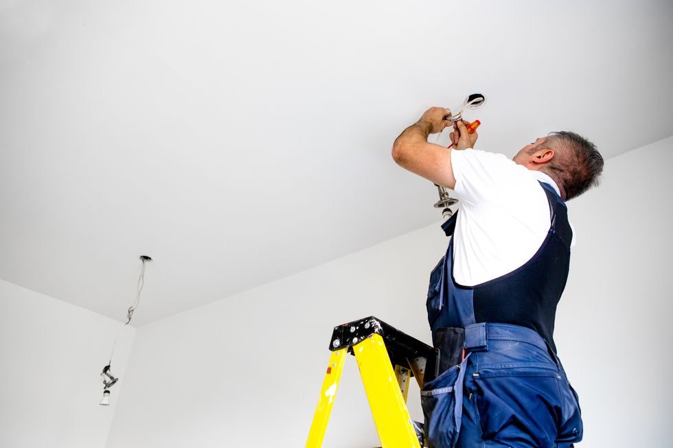 bir tamirci bir erkek elektrikçi tavan armatürüne led ışık takarak ışığı tamir ediyor