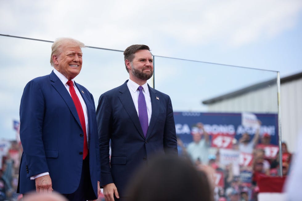 donald trump and jd vance stand together and smile as they look out toward a crowd, both men wear blue suit jackets with white collared shirts and ties