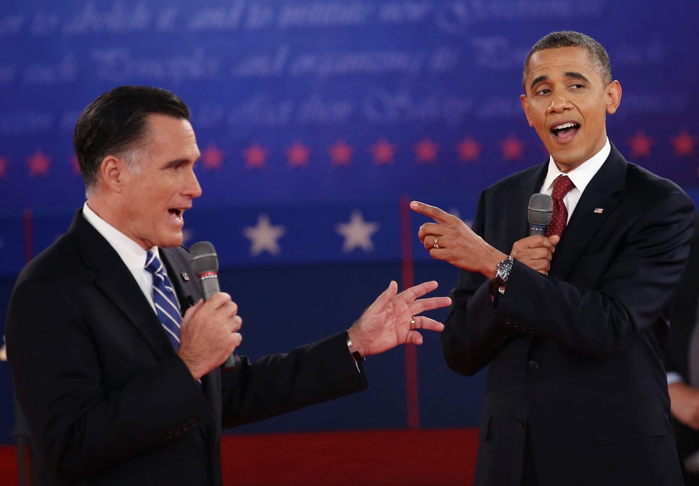 mitt romney and barack obama, both wearing black suits and ties, speak simultaneously into microphones on a stage during a debate