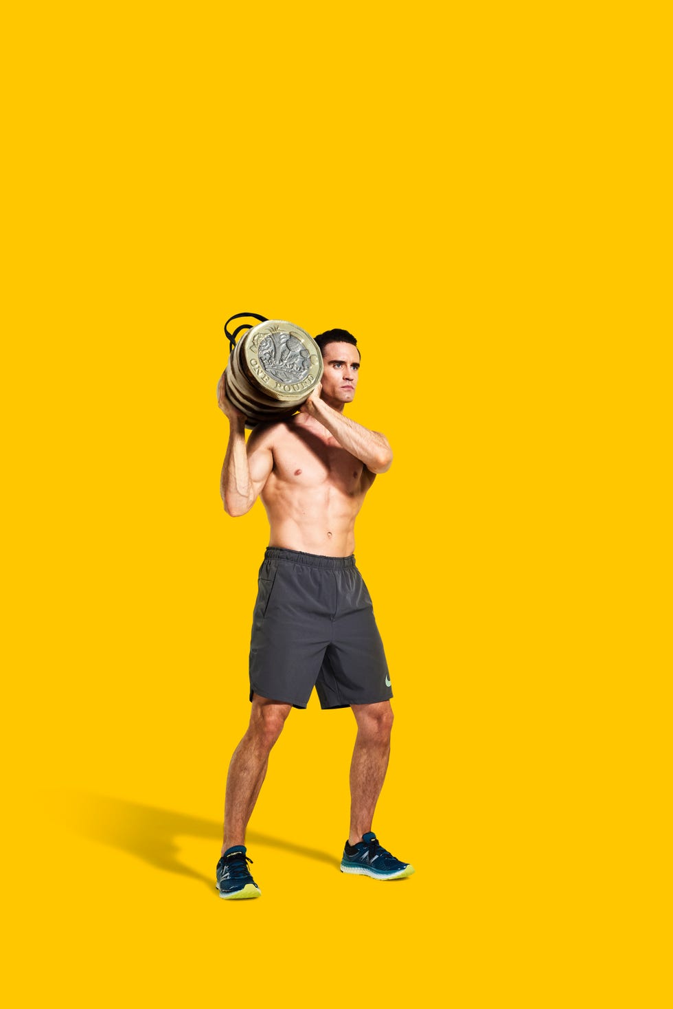 topless male model in black sports shorts demonstrating sandbag over shoulder