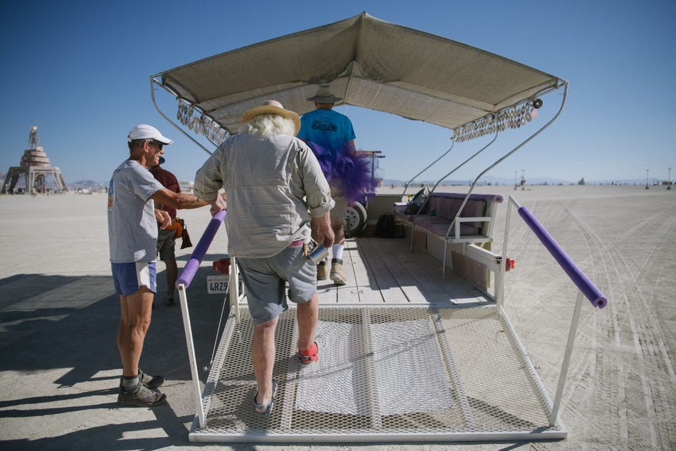 De meeste mensen op Burning Man verplaatsen zich per fiets zelfs over korte afstanden Met ADAvervoer dat toegankelijk is voor rolstoelgebruikers zoals hier op de foto kunnen ook mensen met beperkte mobiliteit naar het achttien vierkante kilometer grote kampeerterrein