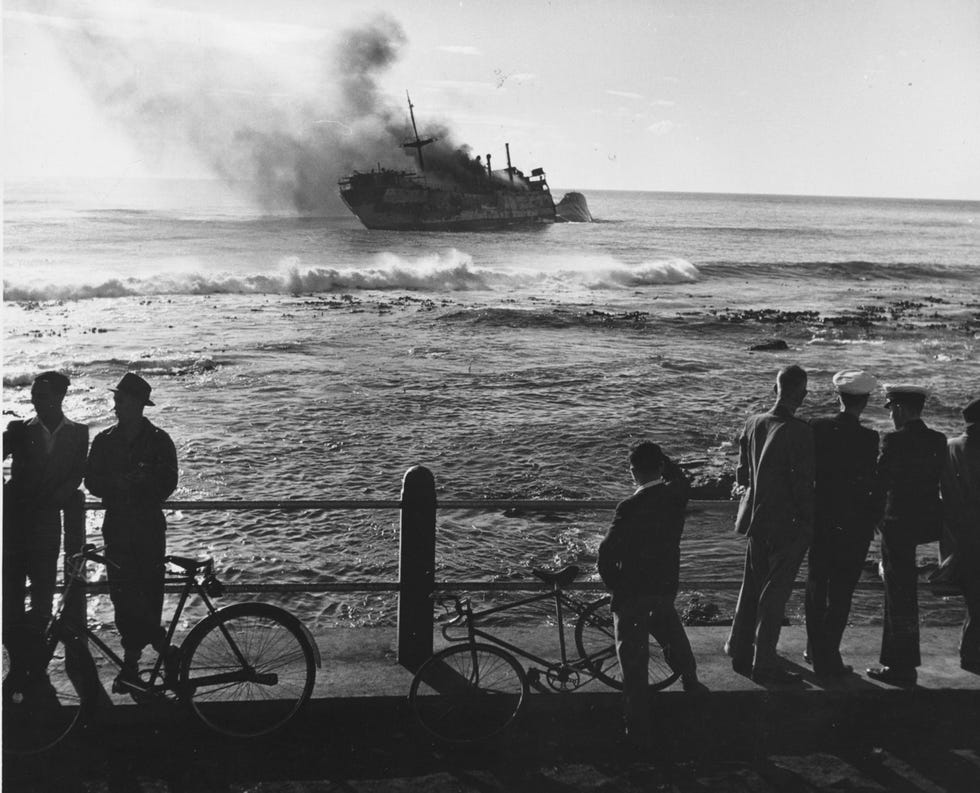 Op de kade bij Kaap de Goede Hoop kijken mensen naar een brand op een schip dat aan de grond gelopen is ca 1950