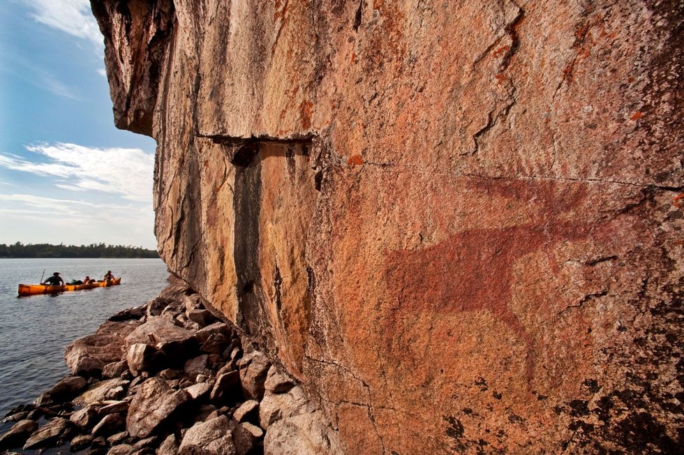 Kanovaarders peddelen langs oude pictogrammen op een rotswand aan de oever van Lac La Croix in de Boundary Waters Canoe Area Wilderness in Minnesota Het gebied telt ruim twintig locaties waar dit soort rotstekeningen zijn te vinden die tussen 500 en 1500 jaar oud zijn