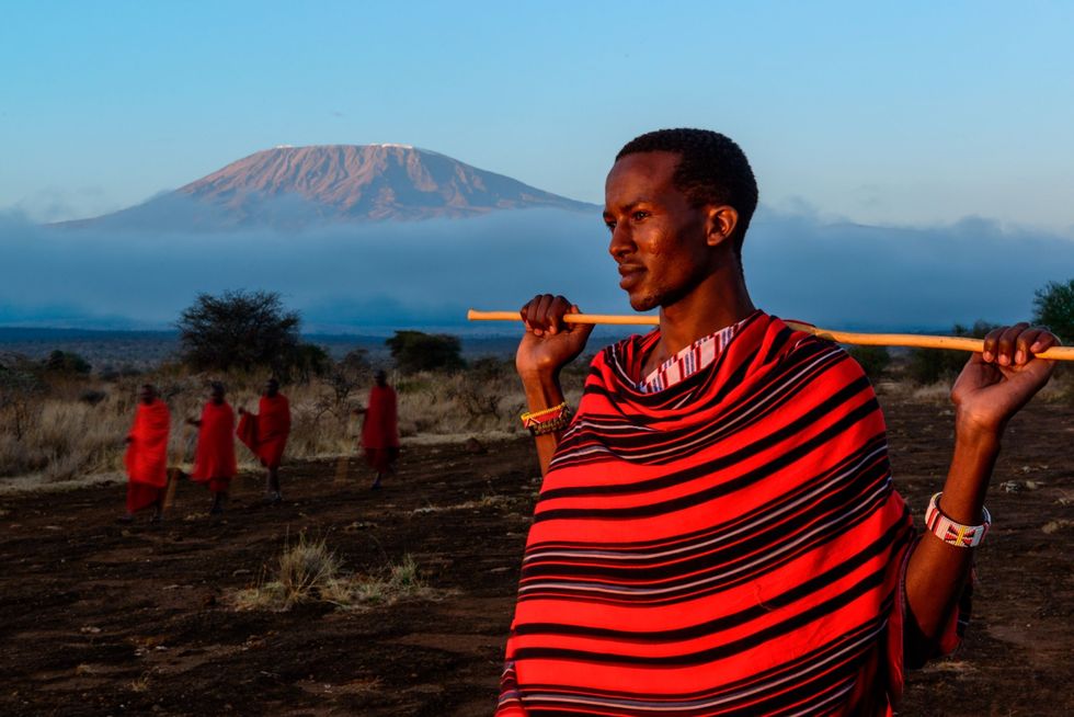 Stamleden van de Maasai lopen door het reservaat van Elerai in de buurt van het Amboseli National ParkinKenia waar de berg Kilimanjaro in de verte verrijst