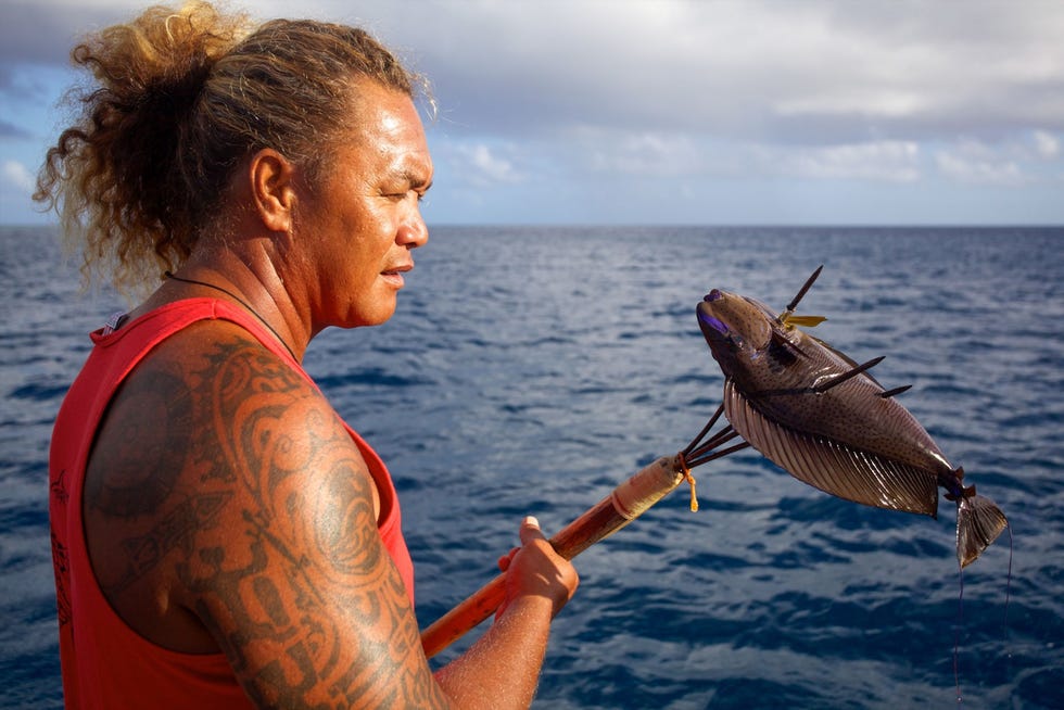 Een man met een tattoo op zijn arm is aan het vissen in Fakarava de grootste atol in FransPolynesi die deel uitmaakt van een UNESCO biosfeerreservaat
