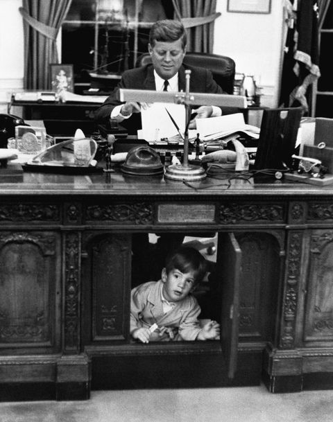 john f kennedy at work at the resolute desk in the oval office of the white house, while his son, john f kennedy jr, hides inside the furnishing