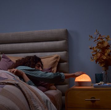 a person lying on a bed reaching for a hatch alarm clock