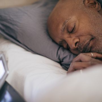 retired senior man sleeping on bed by alarm clock at home