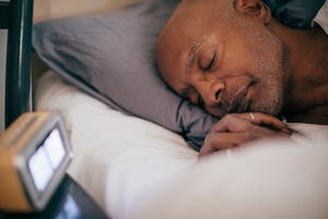 retired senior man sleeping on bed by alarm clock at home