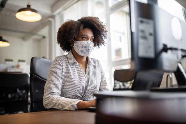 businesswoman with face mask working at her desk looking at computer monitor, in office female professional back to work after covid 19 pandemic lockdown