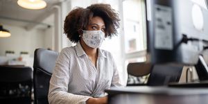 businesswoman with face mask working at her desk looking at computer monitor, in office female professional back to work after covid 19 pandemic lockdown