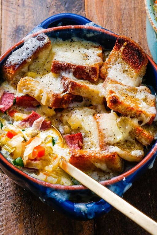 reuben soup topped with cheese in a blue bowl