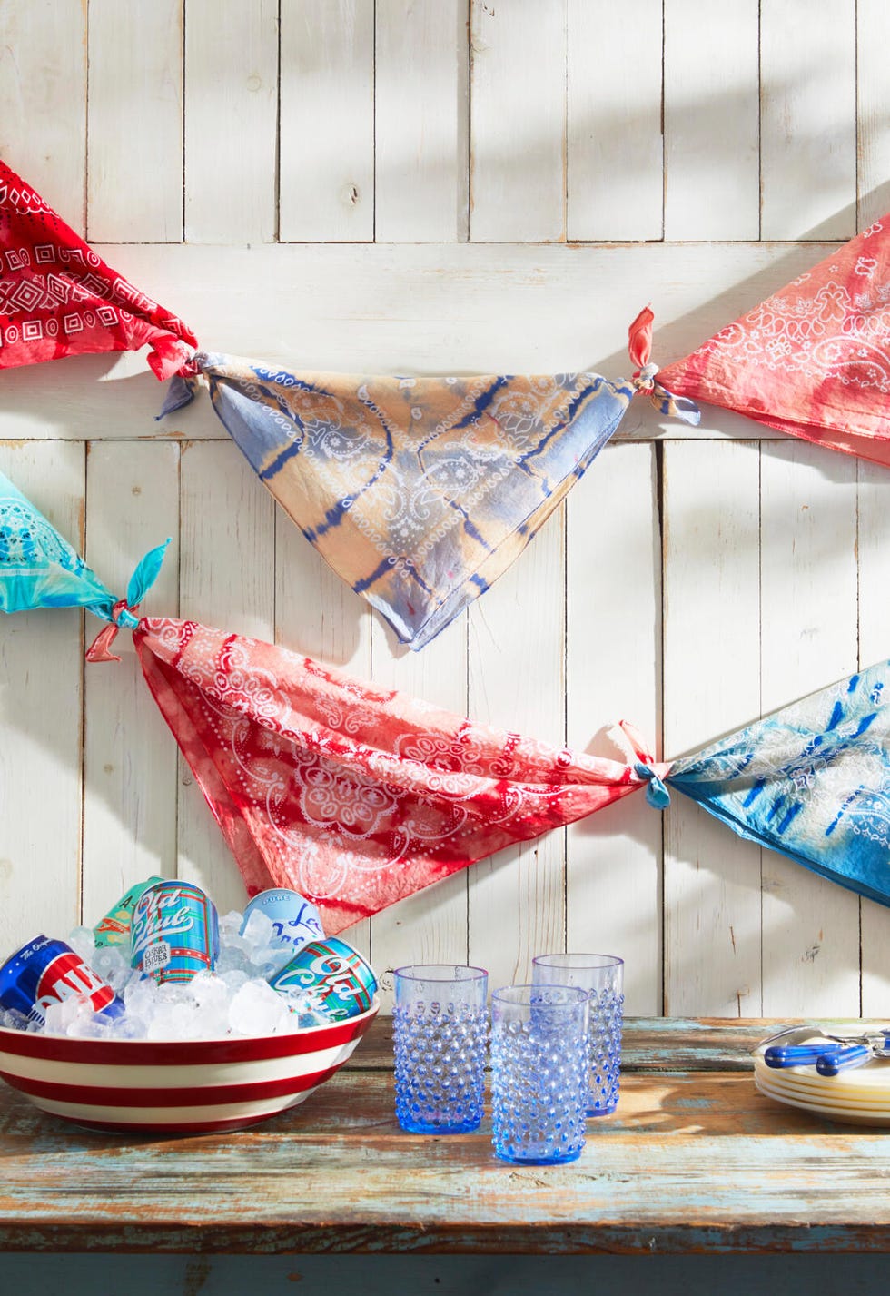 Tie-dyed bandanas tied to bunting hanging on a white wall in front of a table