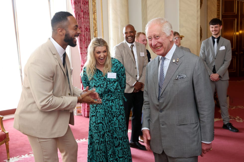 el monarca britanica se divierte con unos jovenes en una recepcion en buckingham