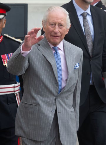 el monarca britanico saluda con la mano con un traje gris de rayas y corbata azul