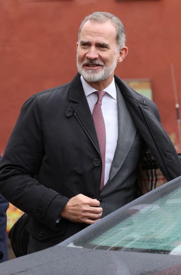 el rey felipe vi sonrie mientras se quita el abrigo