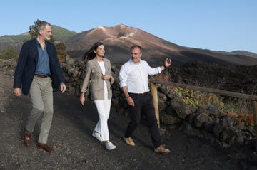 visitors walking along a volcanic landscape with a mountain in the background