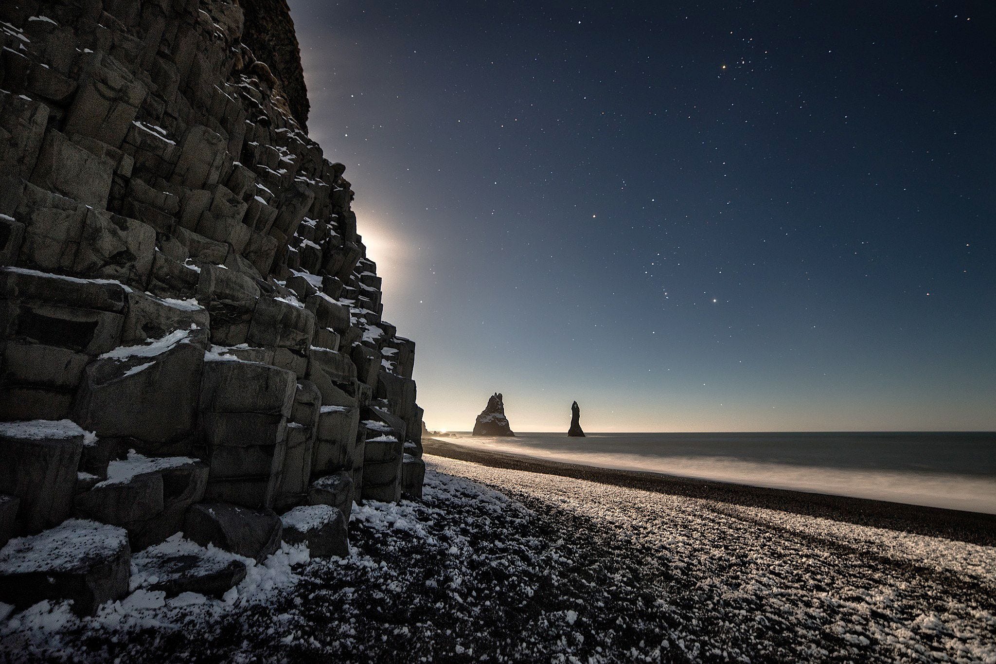 De maan verlicht het strand en de basalten rotstorens bij Reynisfjara op IJsland