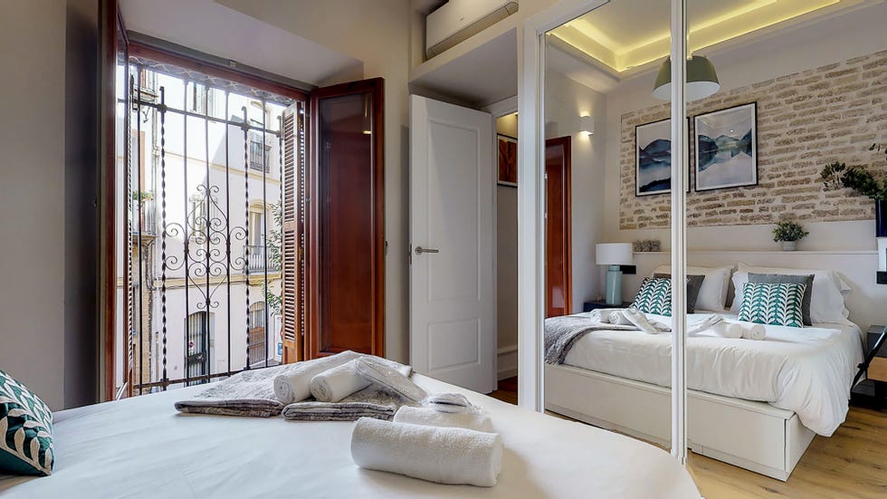 dormitorio con armario con puertas de espejo y pared de ladrillo visto en el cabecero