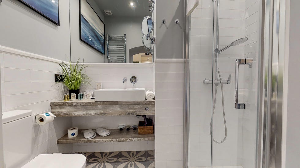 baño con paredes grises revestidas con azulejos blancos y lavamanos flotantes
