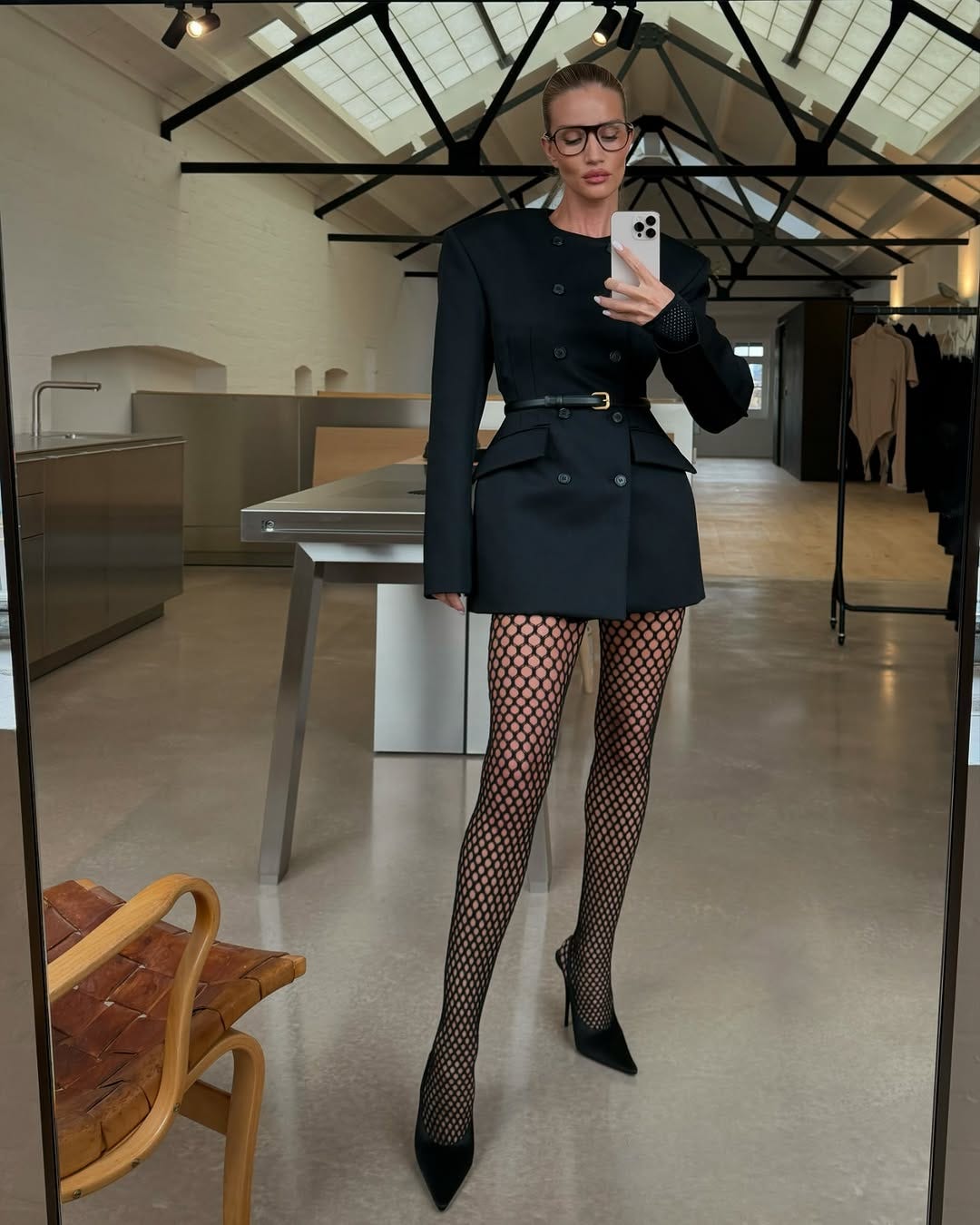 a person wearing a stylish outfit with fishnet tights and high heels stands in a modern interior