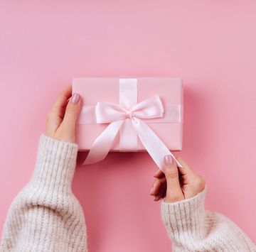 female hands holding a small gift wrapped with pink ribbon