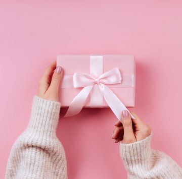 female hands holding a small gift wrapped with pink ribbon