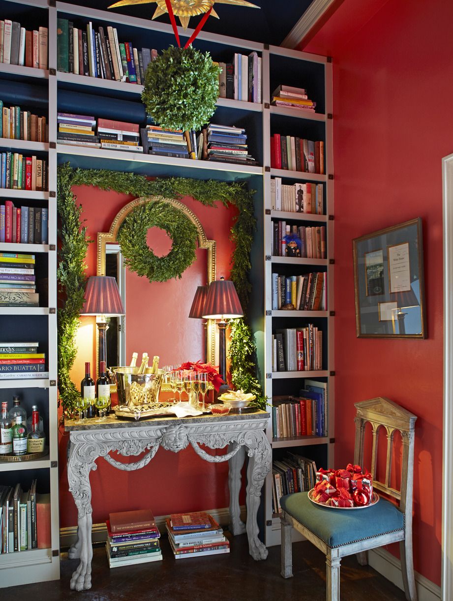 an entry hall with red walls has a console holding glasses of champagne and it is all set for the holidays