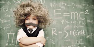 kid dressed like einstein with wig and mustache standing in front of chalkboard covered in equations