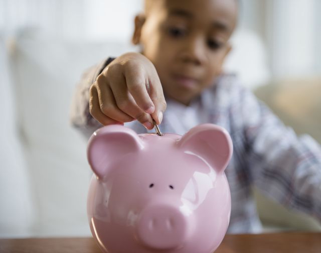 child inserting coin into pink ceramic piggy bank