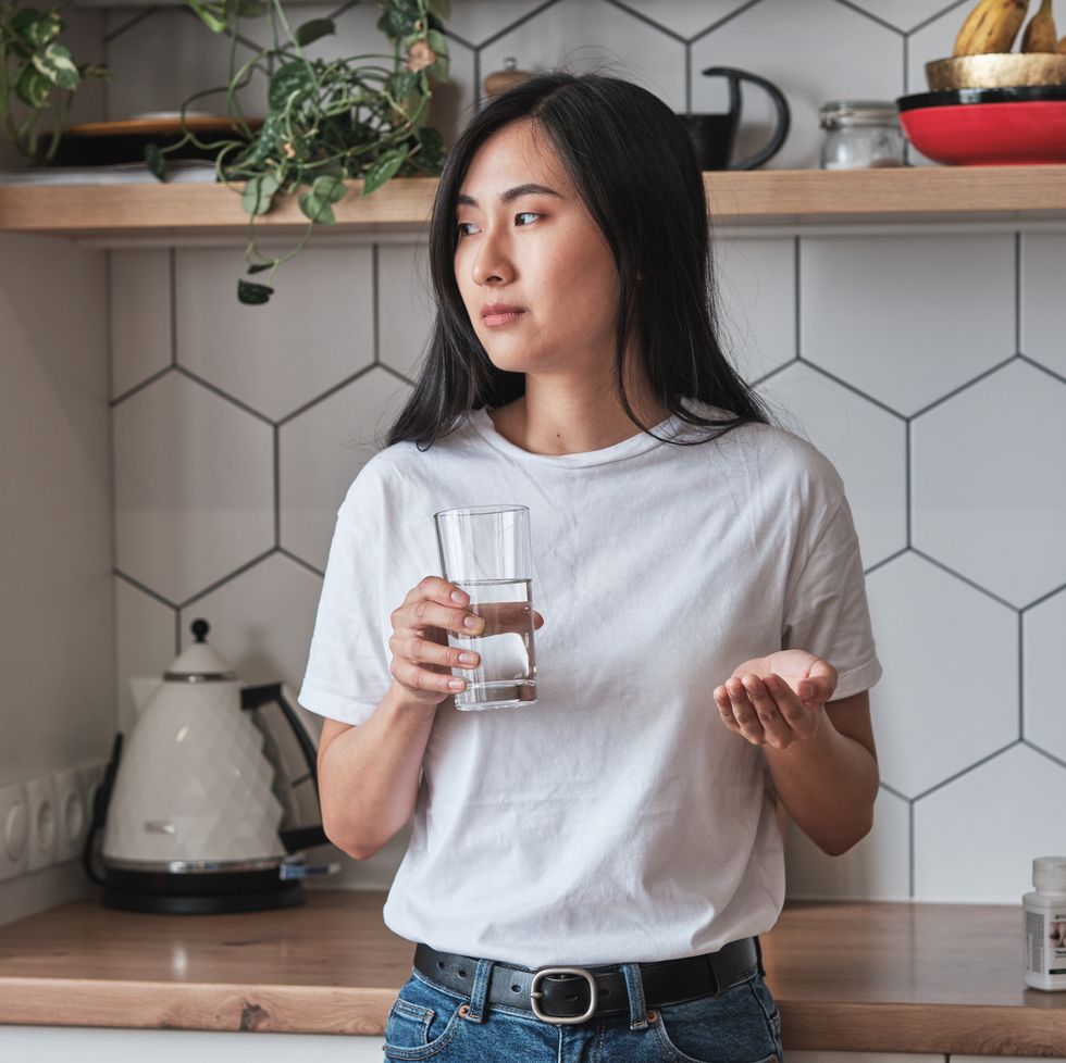 young asian woman holding a glass of water about to take a contraceptive pill