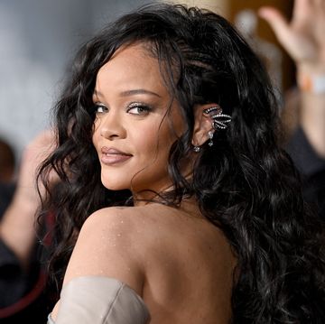 rihanna posing on red carpet with long wavy black hair and off the shoulder dress
