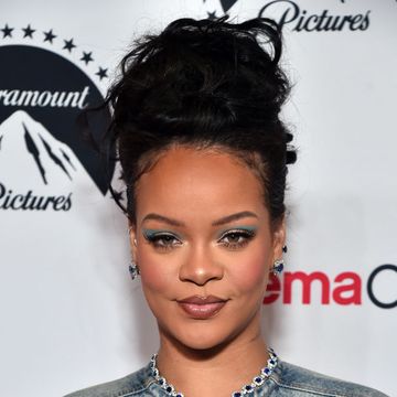 rihanna with her hair up and blue eye makeup poses on a carpet