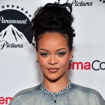 rihanna with her hair up and blue eye makeup poses on a carpet