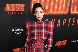 rina sawayama wearing a red pattern dress standing in front of john wick chapter 4 logos