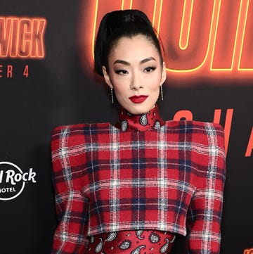 rina sawayama wearing a red pattern dress standing in front of john wick chapter 4 logos