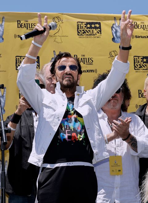 ringo starr holding a microphone and waving to a crowd