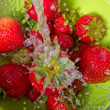 rinsing strawberries in colander under cascading water.