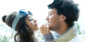 Young woman applying lipbalm to boyfriend's lips, both dressed in winter clothing, side view