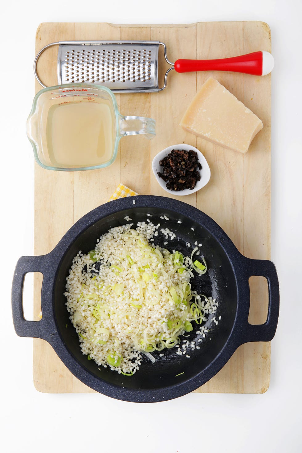 cazuela con arroz, puerro y ajo junto a queso, caldo y rallador