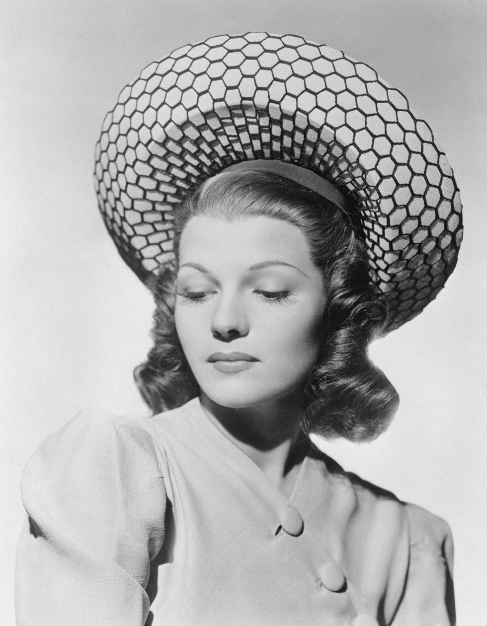 rita hayworth wears a geometric patterned hat and a light colored blouse